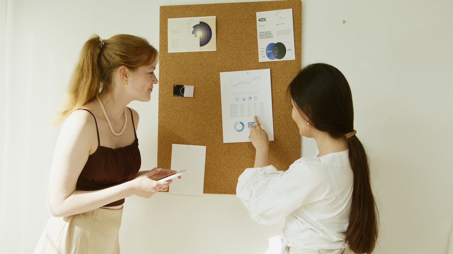 a woman in white long sleeve shirt pointing a graph posted on corkboard